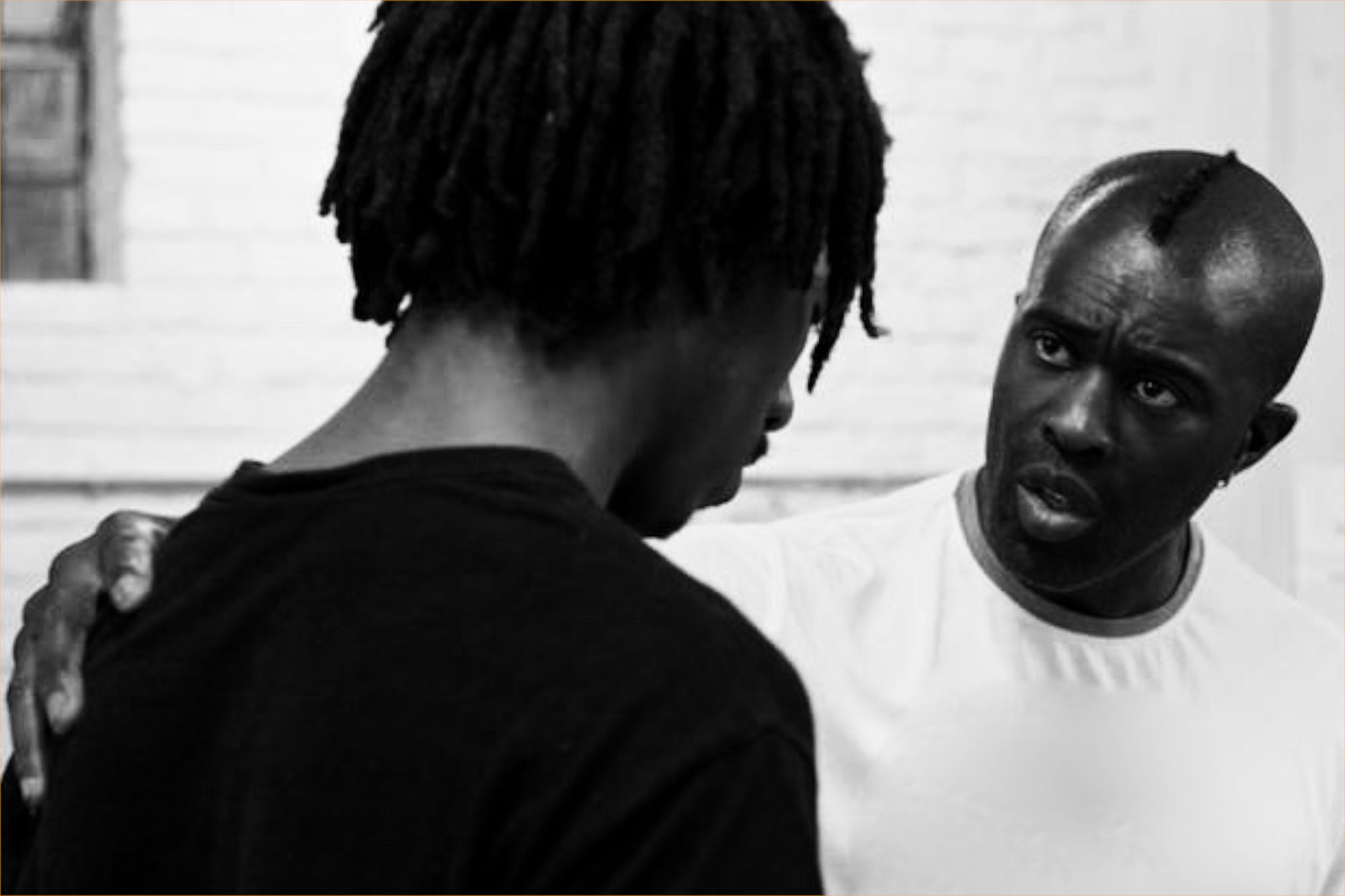 An older black man in a white t-shirt talking to a younger black student in black